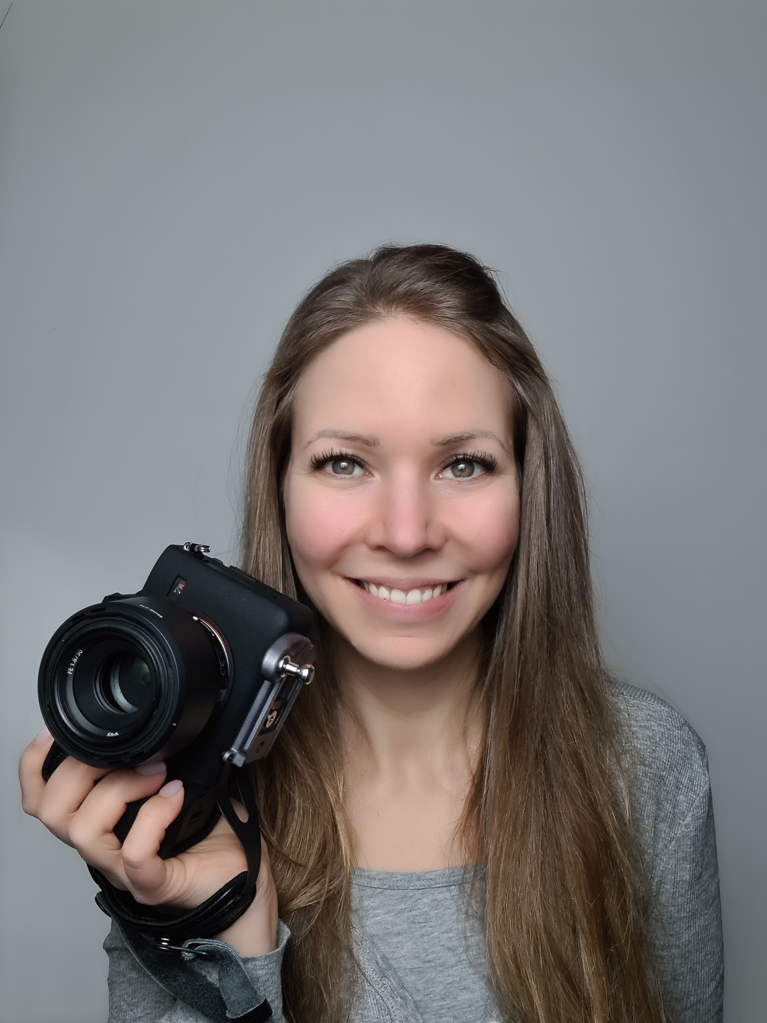 Hochzeitsfotografin mit Kamera in der rechten Hand lächelt den Betrachter an