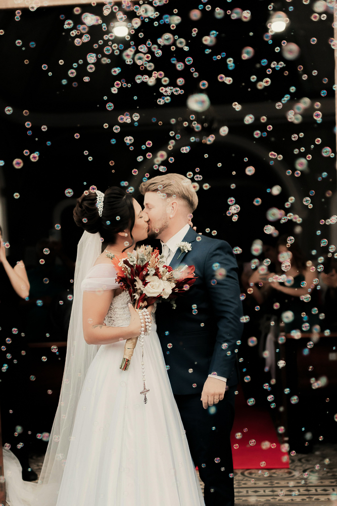 Hochzeitspaar mit Brautstrauß, Hochsteckfrisur, Krone und Schleier kurz nach er kirchlichen Trauung mit Seifenblasen