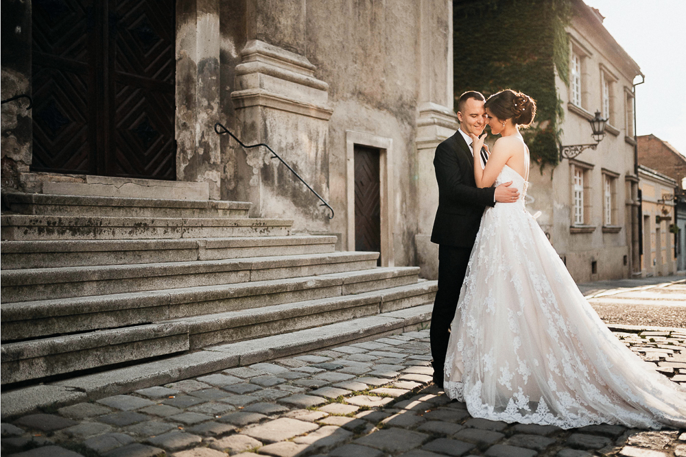 Braut im Fit and Flare Brautkleid mit langer Schleppe und Bräutigam stehen nach ihrer Hochzeit vor einer Treppe zum Brautpaar-Shooting in Wolfsburg.